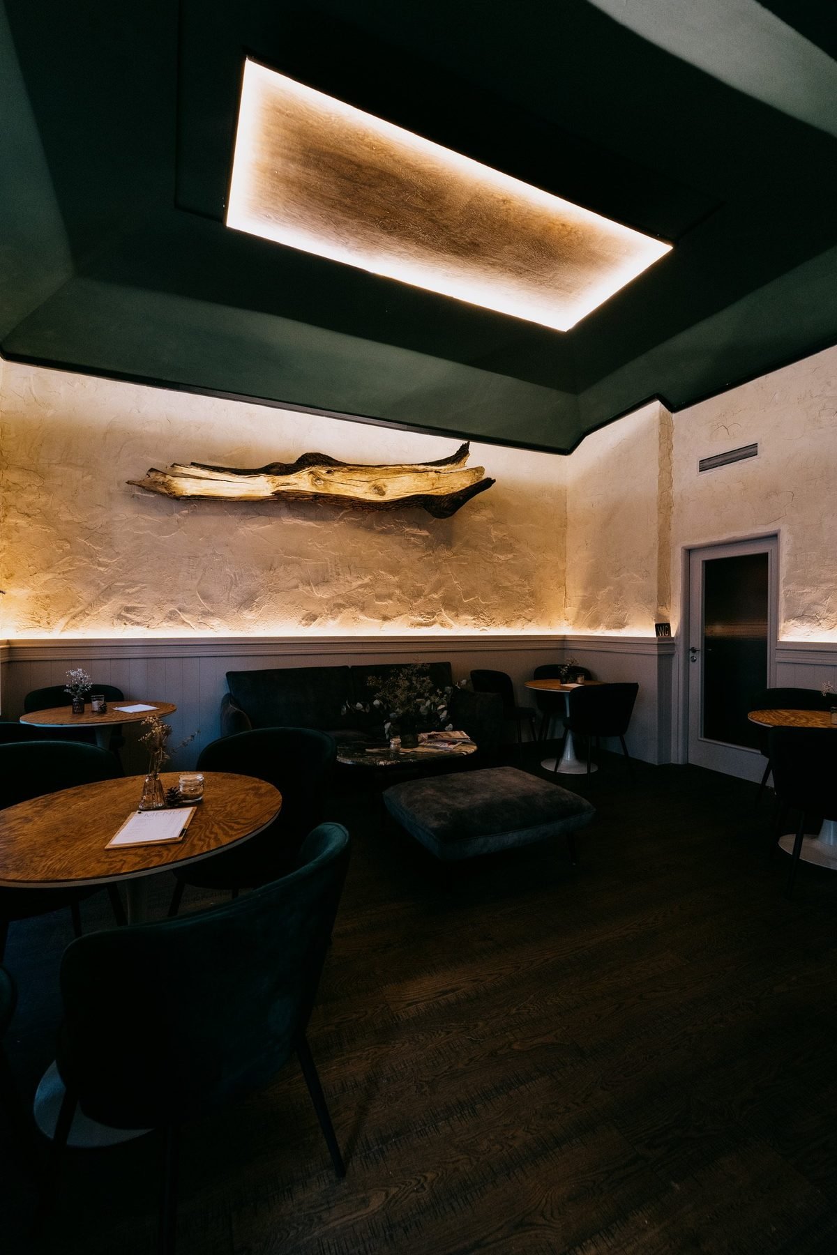 Interiér Wild Cafe – dřevěná plastika pod zeleným stropem, stoly a sametové židle
