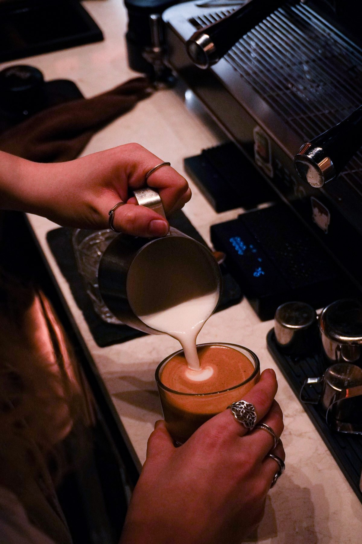 Barista nalévá mléčnou pěnu do flat white – latte art ve Wild Cafe